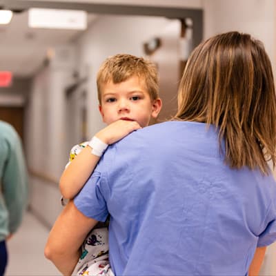 Mother carrying son down hospital hallway.