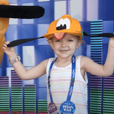 Lily, the Children's Miracle Network Champion, smiling in a picture with Pluto at Disneyland.