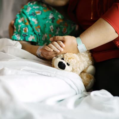 Mother holding the hand of her young child in a hospital bed.
