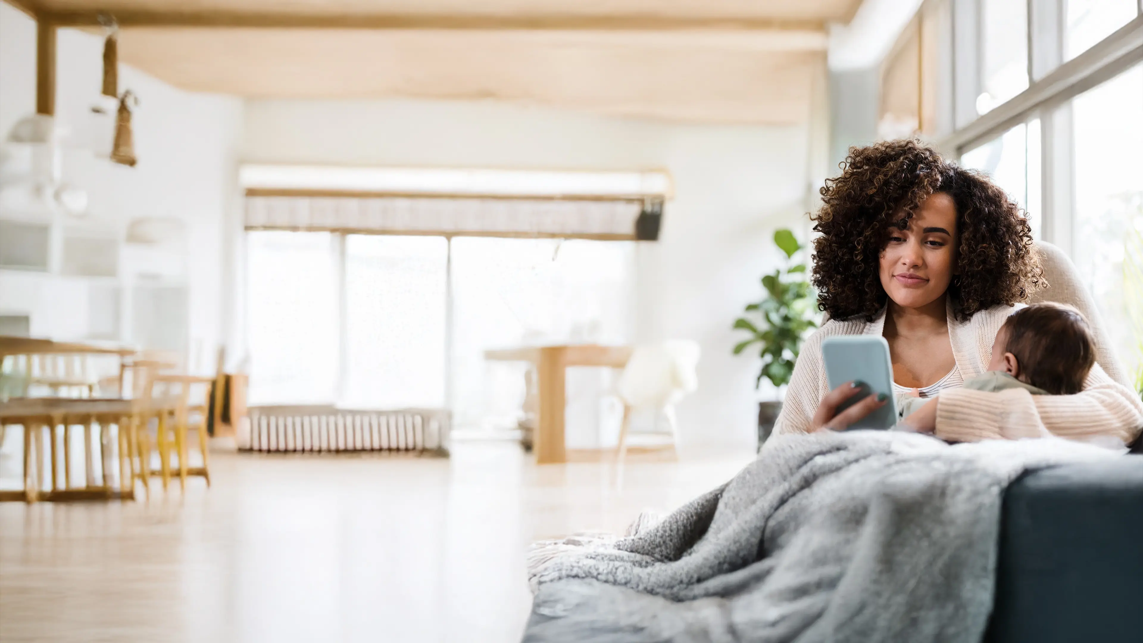 New mom looking at smartphone while holding baby.